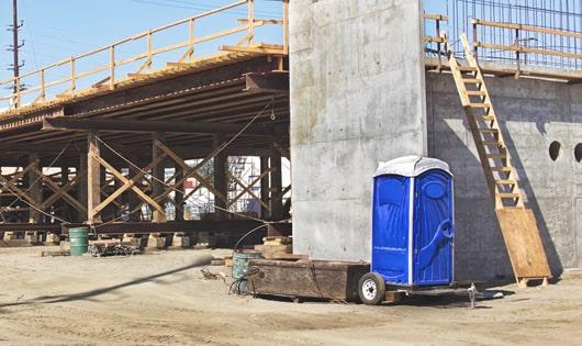 blue portable restrooms arranged in a neat line on a job site